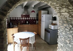 A stone-walled kitchen with a dining table, wooden chairs, a refrigerator, and a dishwasher.