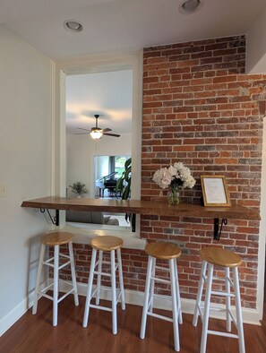 Une cuisine avec un mur en briques, des tabourets de bar en bois et un ventilateur de plafond.