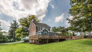 Uma casa de dois andares com varanda, cercada por um gramado e árvores.