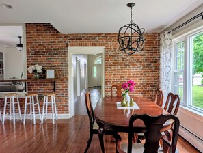 Uma área de refeições com parede de tijolos, mesa de madeira, cadeiras e luminária pendente.