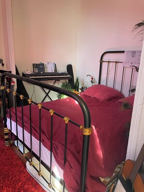 A bed with a red cover, a keyboard on a stand, a bottle, and a plant on a bedside table. - Character house with garden 10 minutes walk from the old town (aix en provence)