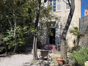 A courtyard with trees, a table, and a chair. - Character house with garden 10 minutes walk from the old town (aix en provence)