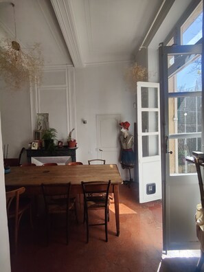 Een eetgedeelte met een houten tafel en stoelen, een witte deur en een uitzicht door een open deur.