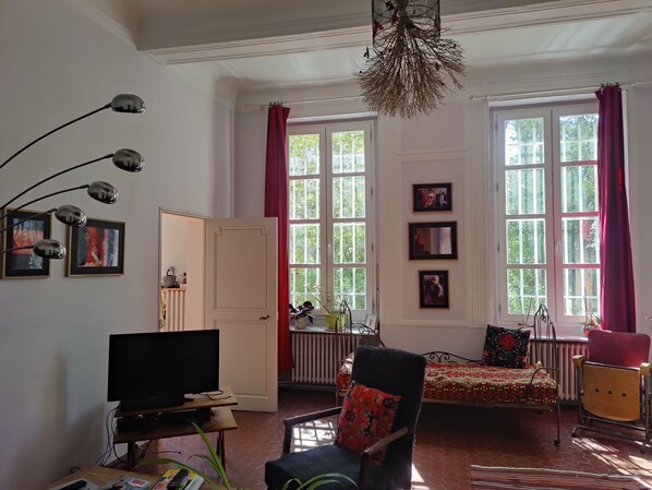 Een woonkamer met een televisie, een stoel, een bed en een raam met gordijnen.
