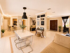 A modern living room with a dining area, a kitchen in the background, and a large window with curtains.