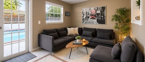 A living room with a grey sofa set, a coffee table, a potted plant, and a pool view through a glass door.