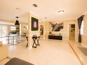 A spacious living area with a dining table, chairs, a sofa, and a decorative wall with a neon sign.