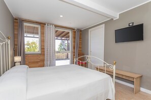 Une chambre à coucher avec un lit, un banc, une télévision et une fenêtre avec des rideaux.