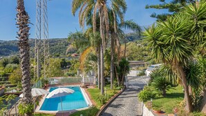 A pool area with a clear blue pool, surrounded by palm trees and a stone pathway. - Apartment in Villa with Pool (Giarre)