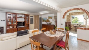 A living room with a sofa, TV, wooden cabinet, dining table, and chairs. - Apartment in Villa with Pool (Giarre)