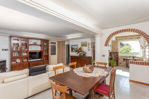 Un salon comprenant un canapé, un téléviseur, un meuble en bois, une table à manger et des chaises.