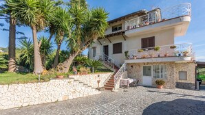 A two-story building with a stone facade, a balcony with potted plants, and a stone staircase leading to the entrance. - Apartment in Villa with Pool (Giarre)