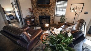 Una sala de estar con chimenea de piedra, sofás de cuero, televisor y una planta grande.