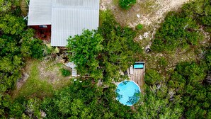 Vista aérea de una propiedad con un edificio de techo metálico, piscina y vegetación densa alrededor.