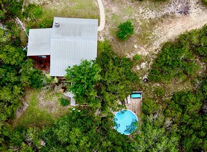 Eine Vogelperspektive zeigt ein Anwesen mit einem Gebäude mit Metallbedachung, einem Swimmingpool und dichter umliegender Vegetation.