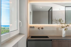 Ein modernes Badezimmer mit einem großen Spiegel, einem Waschbecken und einer Vase mit Pflanzen.