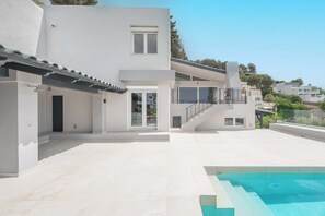 Ein modernes, zweistöckiges Gebäude mit Swimmingpool, einer überdachten Terrasse und einer Treppe, die zum Obergeschoss führt.