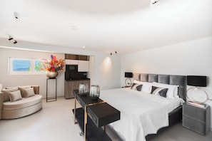 Ein modernes Schlafzimmer mit Bett, Nachttischen, einer Couch, einer Küchenzeile und Blick auf die Stadt.