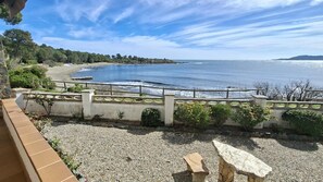 Blick auf die Küste mit einem Kiesstrand, einem Holzzaun und einer Steinsitzbank.