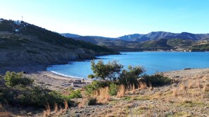 Eine Küstenlandschaft mit Strand, felsigem Gelände und Bergen im Hintergrund.