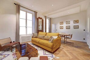 A living room with a sofa, coffee table, and a dining area with a table and chairs. - ELEGANT 3BR APARTMENT WITH ENSUITE BATHS NEAR CANAL SAINT-MARTIN (Paris)