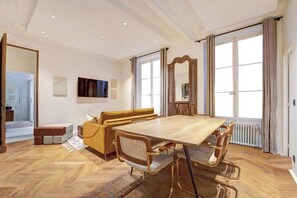 A spacious room with a wooden dining table, a sofa, and a large mirror. - ELEGANT 3BR APARTMENT WITH ENSUITE BATHS NEAR CANAL SAINT-MARTIN (Paris)
