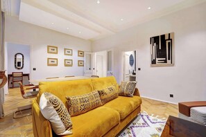 A spacious living area with a yellow sofa, framed pictures on the wall, and a modern abstract painting. - ELEGANT 3BR APARTMENT WITH ENSUITE BATHS NEAR CANAL SAINT-MARTIN (Paris)
