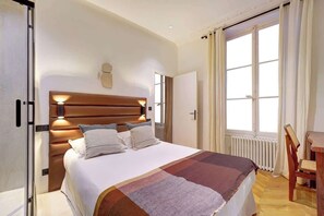 Et hotelværelse med en stor seng, et træhovedgærde, et natbord, en stol, et vindue med gardiner og en radiator.