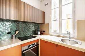 A kitchen with a modern design, featuring a green tiled backsplash, a stainless steel sink, and a window providing natural light. - ELEGANT 3BR APARTMENT WITH ENSUITE BATHS NEAR CANAL SAINT-MARTIN (Paris)