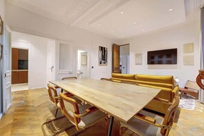 A spacious room with a large wooden dining table, comfortable seating, and a modern kitchen area. - ELEGANT 3BR APARTMENT WITH ENSUITE BATHS NEAR CANAL SAINT-MARTIN (Paris)