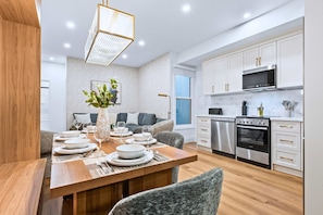 Una cocina moderna con armarios blancos, electrodomésticos de acero inoxidable y un comedor con una mesa de madera para cuatro.