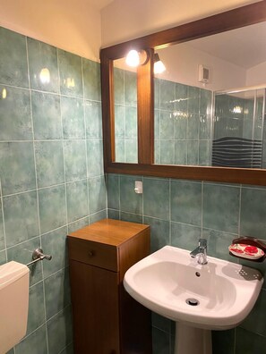 A bathroom with a white sink, wooden cabinet, and green tiled walls. - Vrbo Property (Cagli)