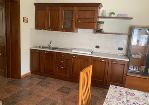 Een keuken met houten kastjes, een spoelbak en een eettafel met stoelen.