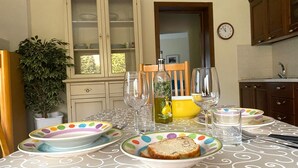 A dining table set with plates, glasses, and a bottle, with a cabinet and a clock in the background. - Il Bosso Apartment in Cagli with a 15x6m saltwater pool (Cagli)