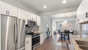 A modern kitchen with stainless steel appliances, white cabinetry, and a dining area with a stone countertop. - 3BR Home Downtown Atlanta | BeltLine | Mozley Park (Atlanta)