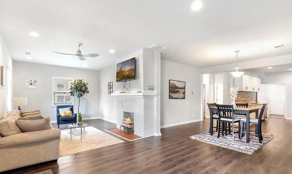 A spacious living room with a fireplace, a dining area with a table and chairs, and a kitchen in the background. - 3BR Home | Minutes to World Cup & BeltLine (Atlanta)
