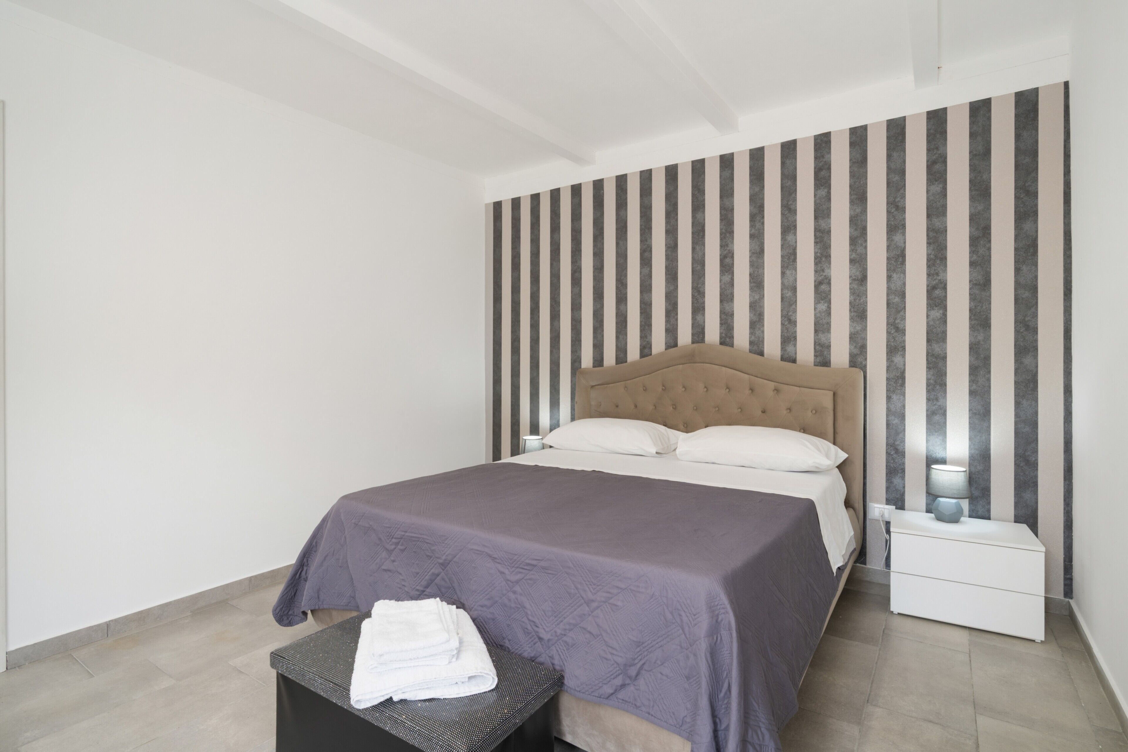 Une chambre à coucher moderne avec un lit, une table de chevet et un banc avec des serviettes.