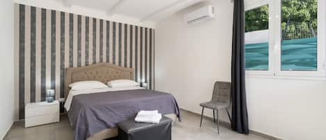 A modern bedroom with a bed, bedside tables, a chair, and a window with a view.