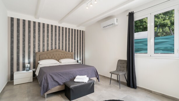 A modern bedroom with a bed, bedside tables, a chair, and a window with a view.