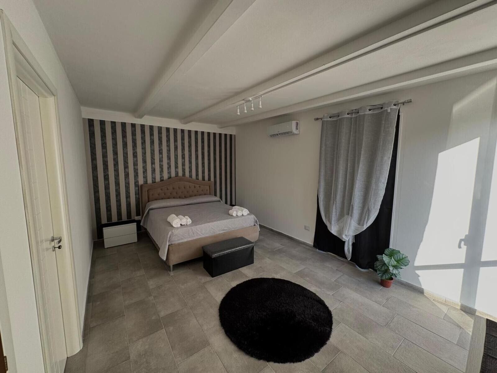Una camera da letto con un letto, un tappeto nero, una pianta in vaso e una finestra con tende.. Appartamento 'Camera Luna' con piscina condivisa, Wi-Fi e aria condizionata