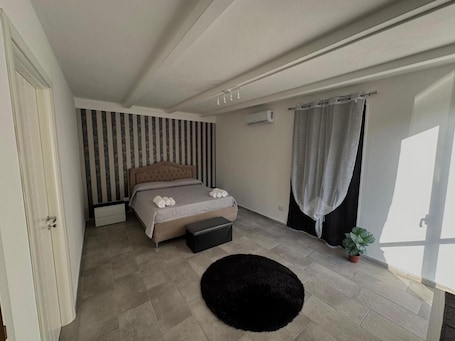 Una camera da letto con un letto, un tappeto nero, una pianta in vaso e una finestra con tende.. Appartamento 'Camera Luna' con piscina condivisa, Wi-Fi e aria condizionata