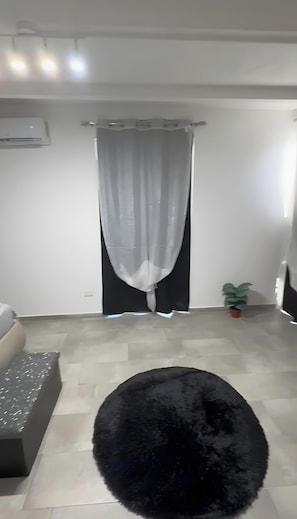 A modern living room with a black furry rug, a grey sofa, a potted plant, and a window with sheer curtains.