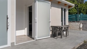 A modern building with a sliding glass door entrance, a patio area with a table and chairs, and a statue.