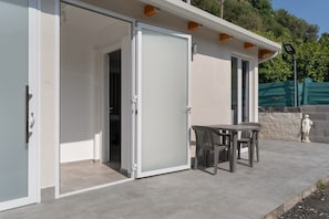 Un bâtiment moderne doté d’une entrée avec une porte vitrée coulissante, d’un patio avec une table et des chaises, et d’une statue.