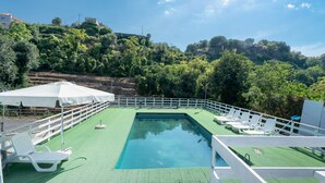 A swimming pool with a surrounding deck, white lounge chairs, and a white fence.