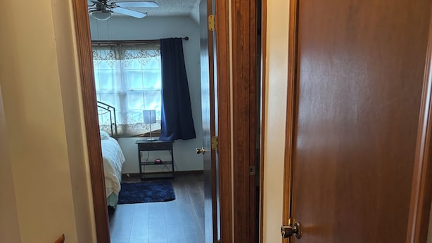 Un pasillo estrecho que conduce a un dormitorio con cama, mesita de noche y ventilador de techo.