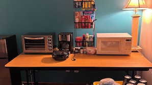 Una kitchenette con tostadora, cafetera, microondas y un estante con diversos productos alimenticios.