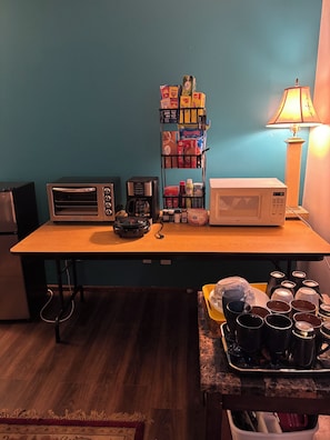 A kitchenette with a toaster, coffee maker, microwave, and a shelf with various food items. - Peace, family friendly, business vacation home. (Lawrence)