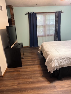 Een slaapkamer met een bed, een televisie op een standaard en een raam met gordijnen.