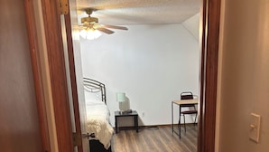 Un dormitorio con cama, mesita de noche, escritorio y ventilador de techo.